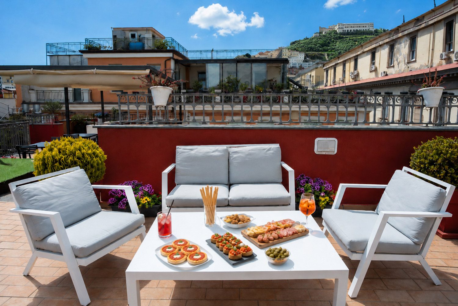 White outdoor sofas beside a red parapet overlooking nearby rooftops.