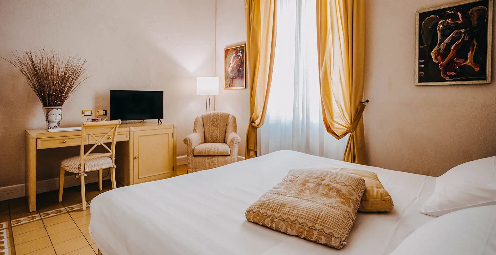 Classic bedroom with yellow curtains, a writing desk and framed artwork.