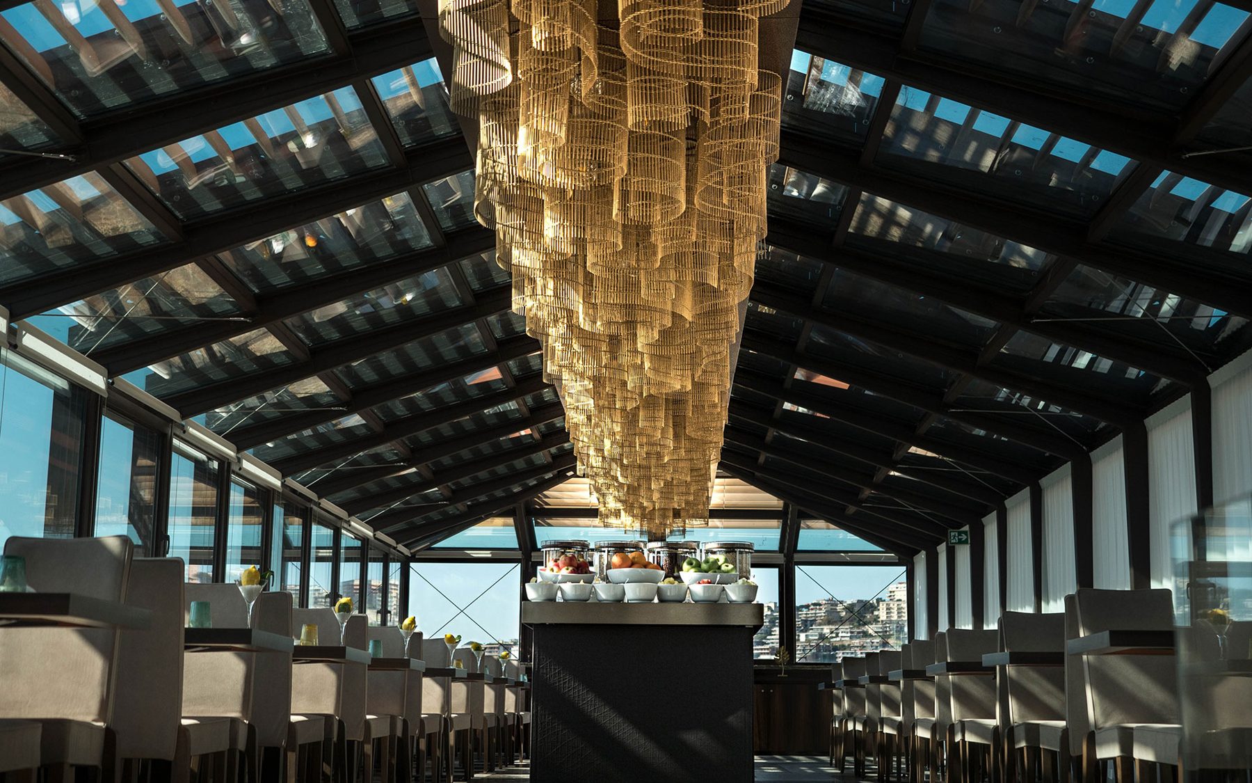 Dining room beneath a glazed roof and a suspended gold-toned installation.