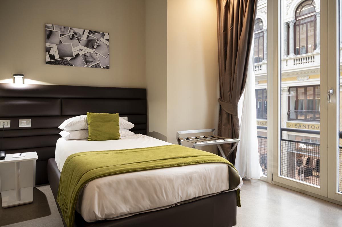 Bedroom with green bedding, dark headboard and tall windows facing the Galleria.