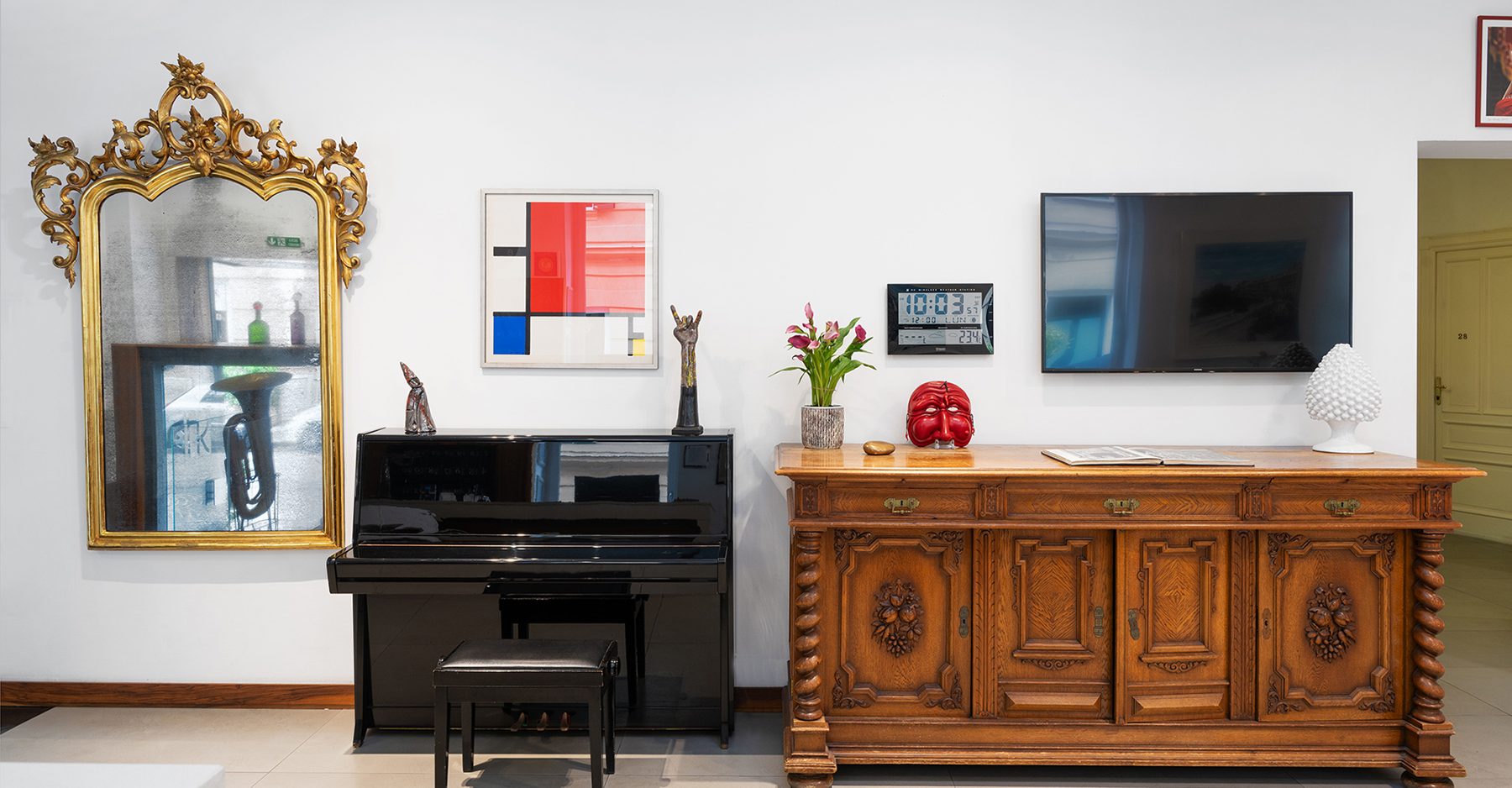 Piano and carved wooden sideboard beneath a mirror and artwork.