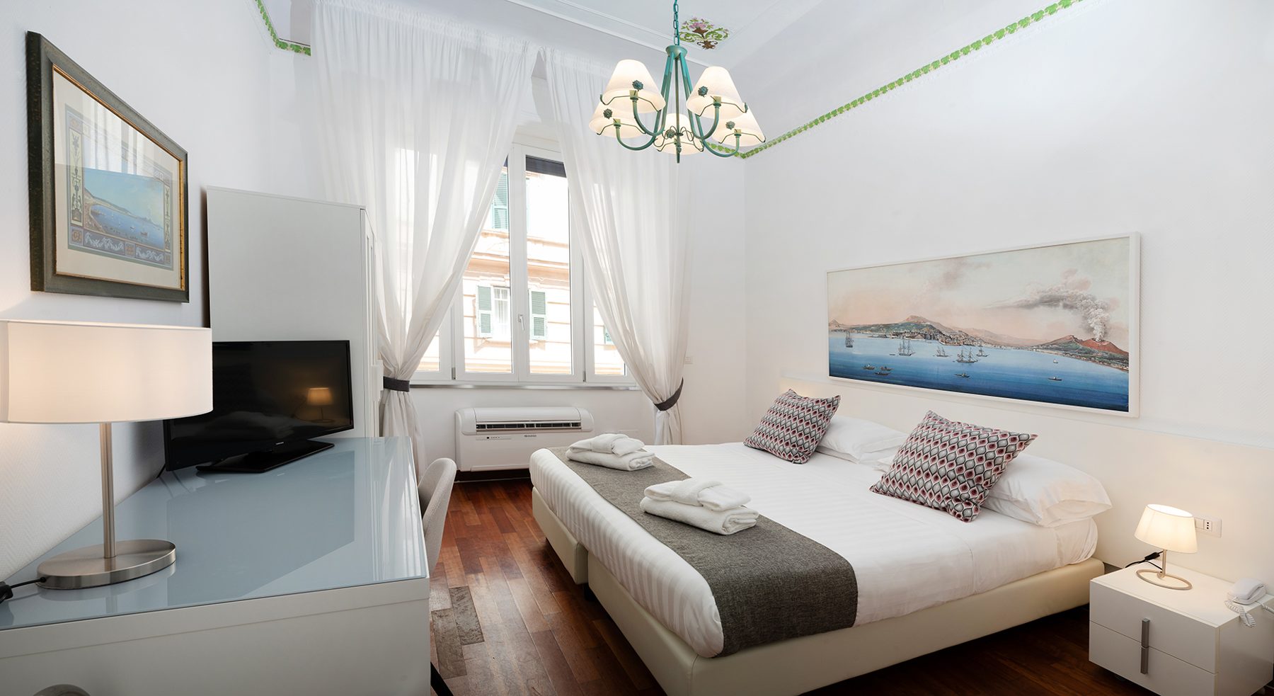 Bedroom with a window, pale curtains and a framed bay picture above the bed.