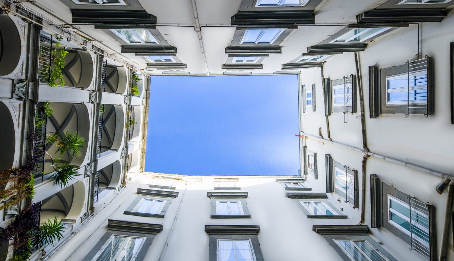 White courtyard walls and green shutters framing a square of sky.