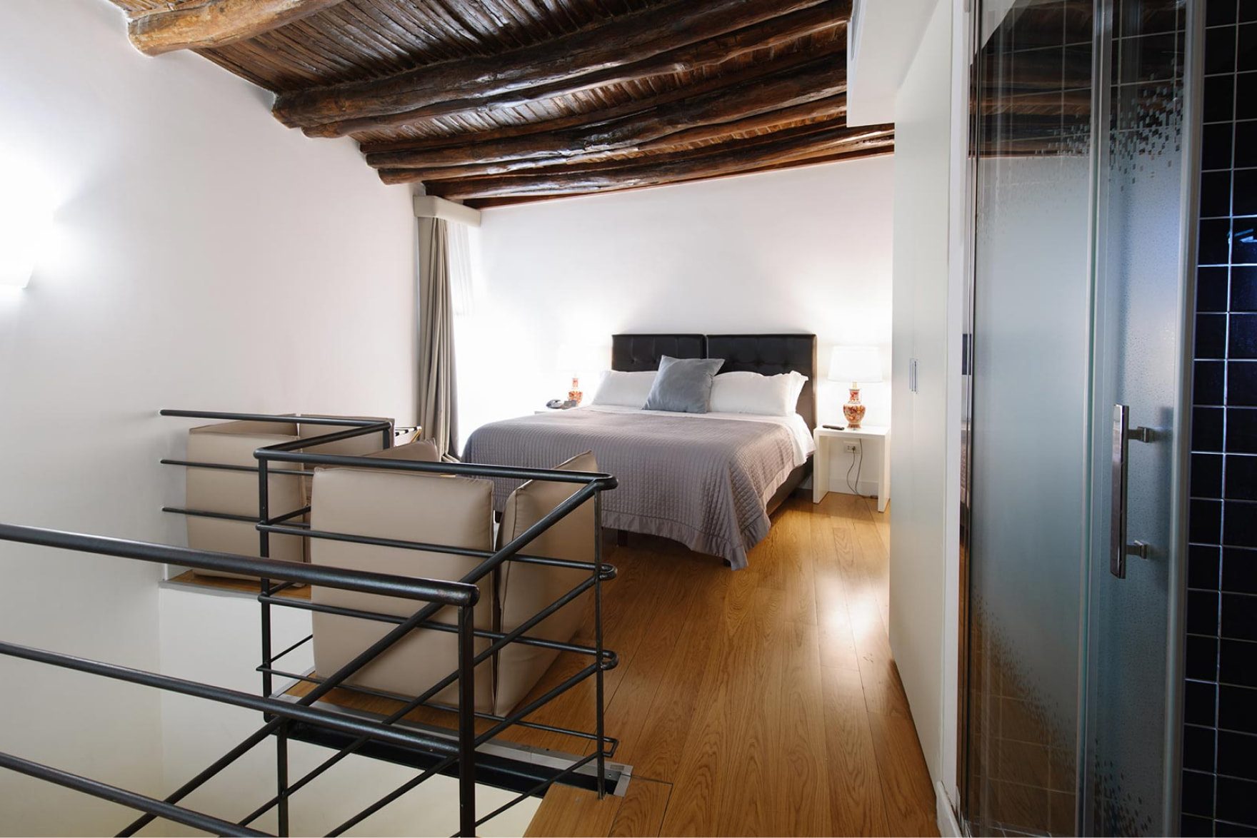 Mezzanine bedroom beneath exposed beams, with a stair railing.