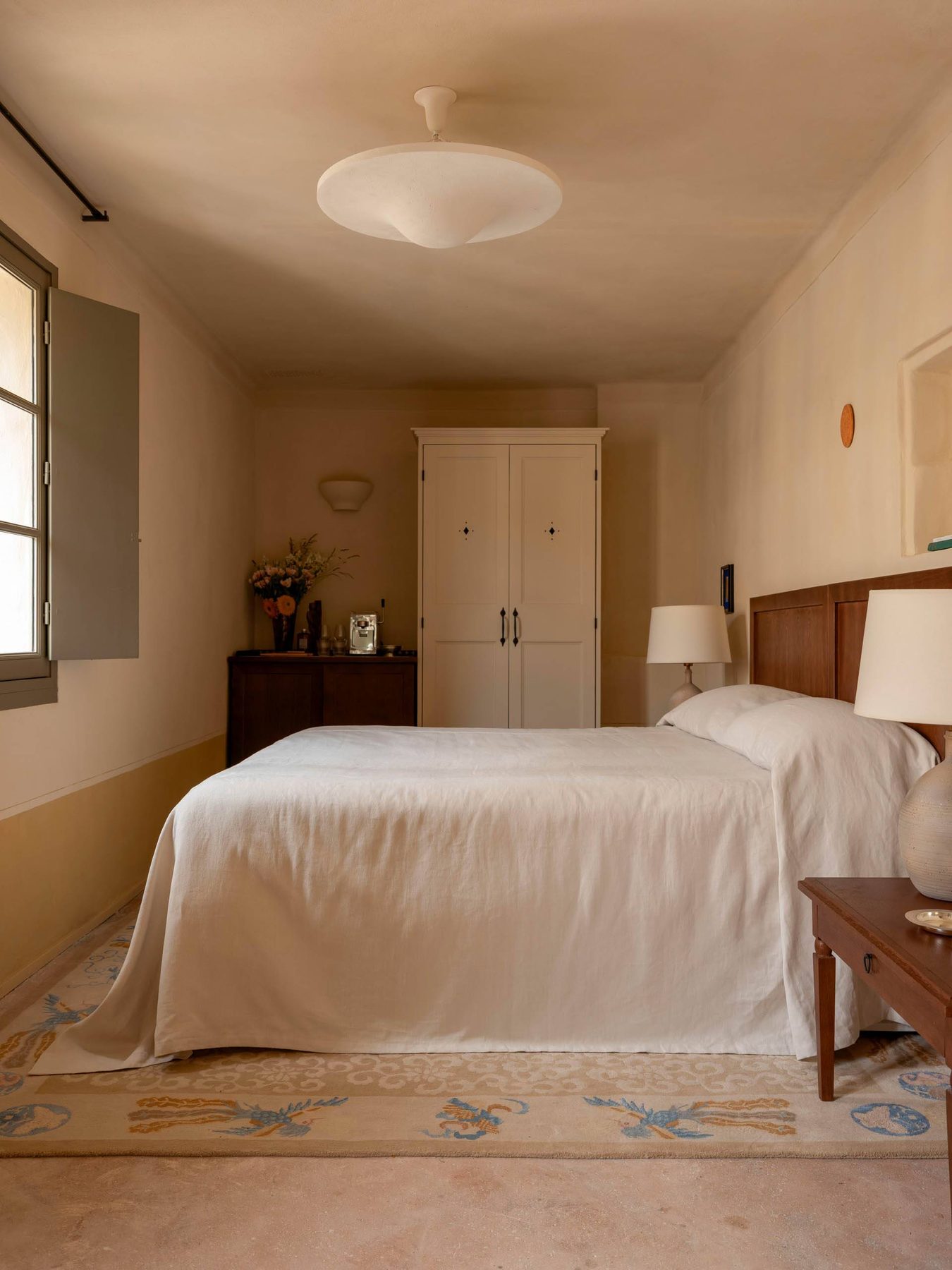 Double bed beneath a pendant light in a pale-toned Capucines room