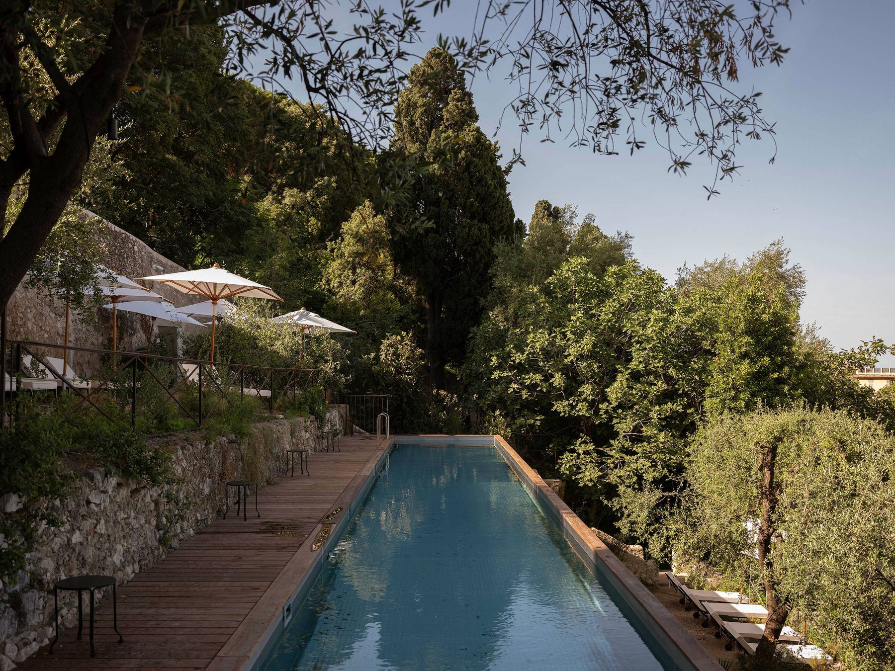 Long outdoor swimming pool beside a stone wall and trees at Hôtel du Couvent