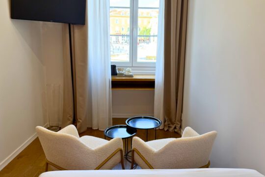 Two chairs and small round tables beside the window at Hôtel de la Mer