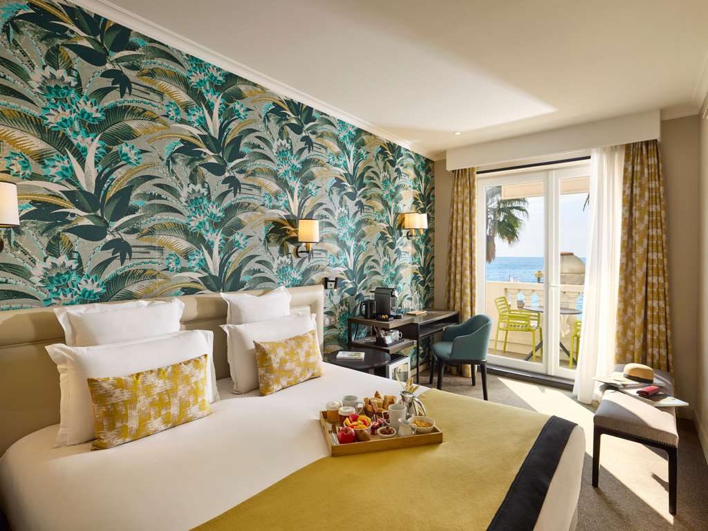 Double bed with leaf-patterned wallpaper and a balcony doorway at Mercure Marché aux Fleurs
