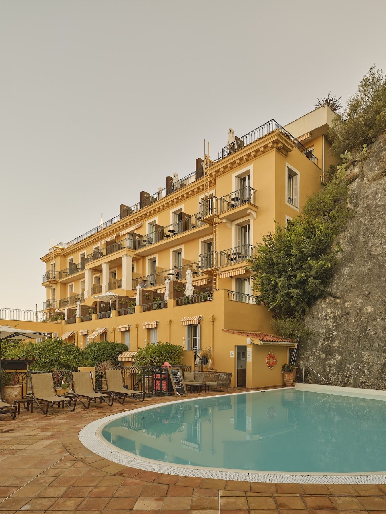 Outdoor swimming pool beside the hotel building and planted hillside at La Pérouse