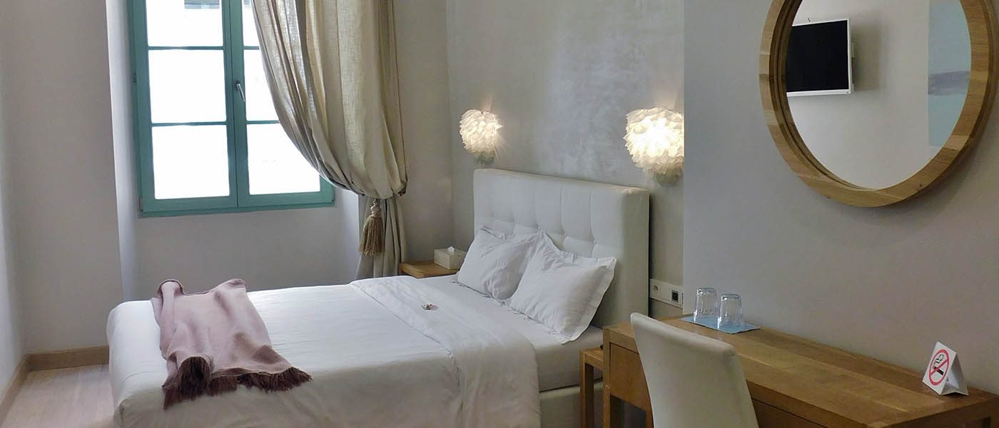 Light-toned bedroom with a desk, round mirror and tall window at Hôtel Rossetti