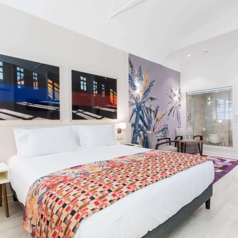 Bed with patterned cover beneath framed pictures in a Palais Saleya Junior Suite