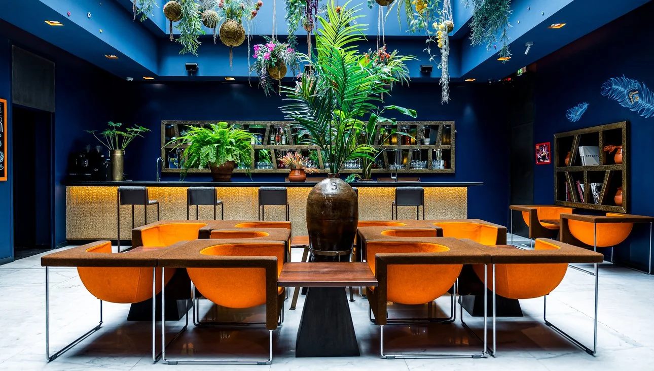 Blue walls, orange chairs and planting in a shared space at 1K Paris.