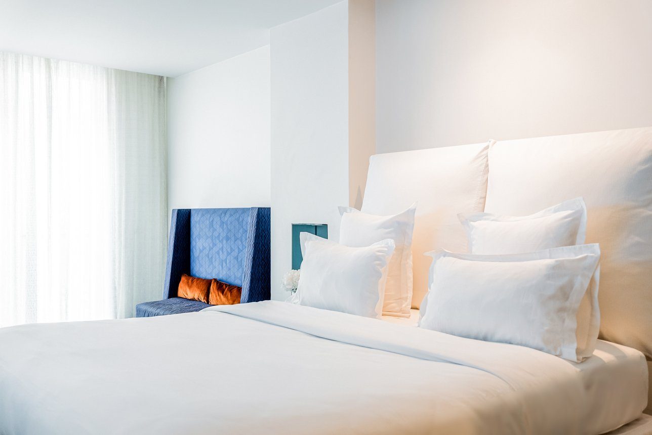 White bed and a blue chair in 1K Paris’ XL Junior Suite.