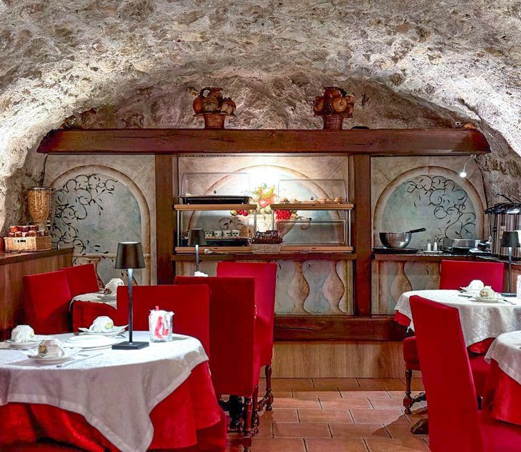 Red chairs and set tables under a stone vault at Hôtel de la Bretonnerie.