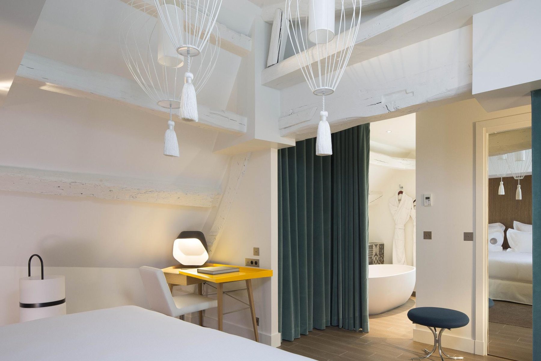 Light bedroom with yellow desk and a bathroom doorway at Hôtel Dupond-Smith.