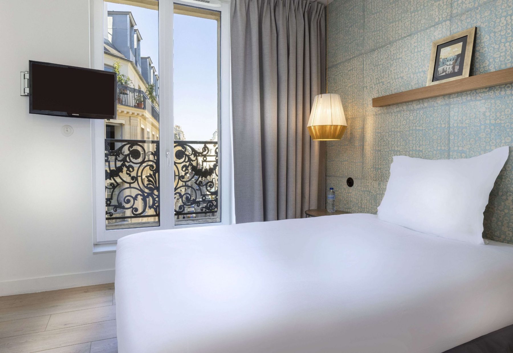 White bed beside a window and pendant light at Hôtel Emile.
