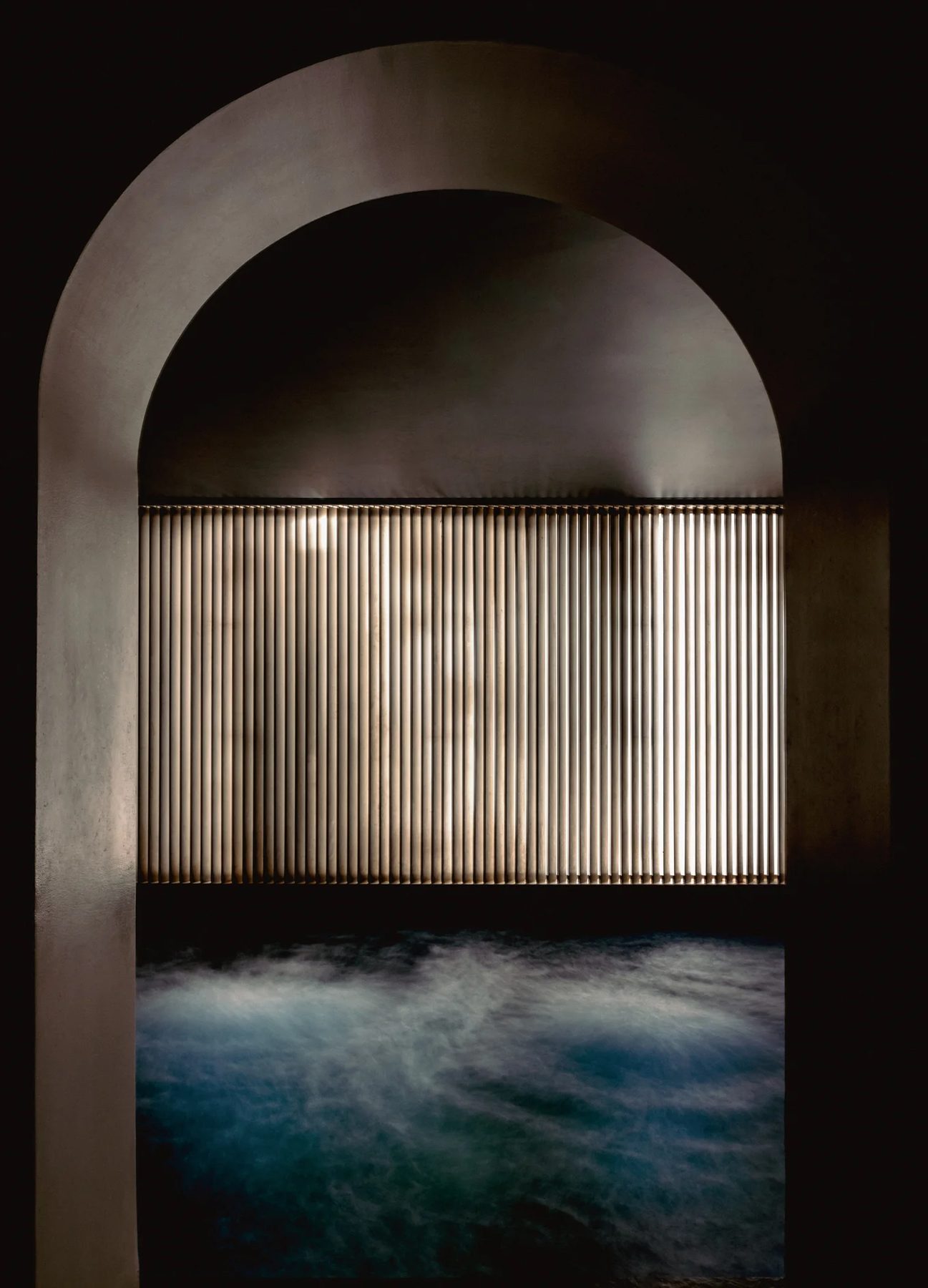 Blue water beneath a dark arch in Experimental Marais’ Roman bath.
