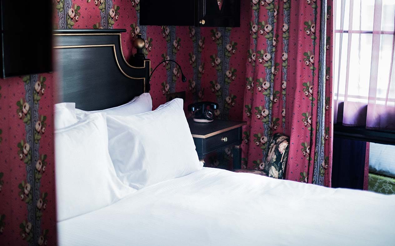 White bed, black headboard and pink floral walls at Hôtel de JoBo.