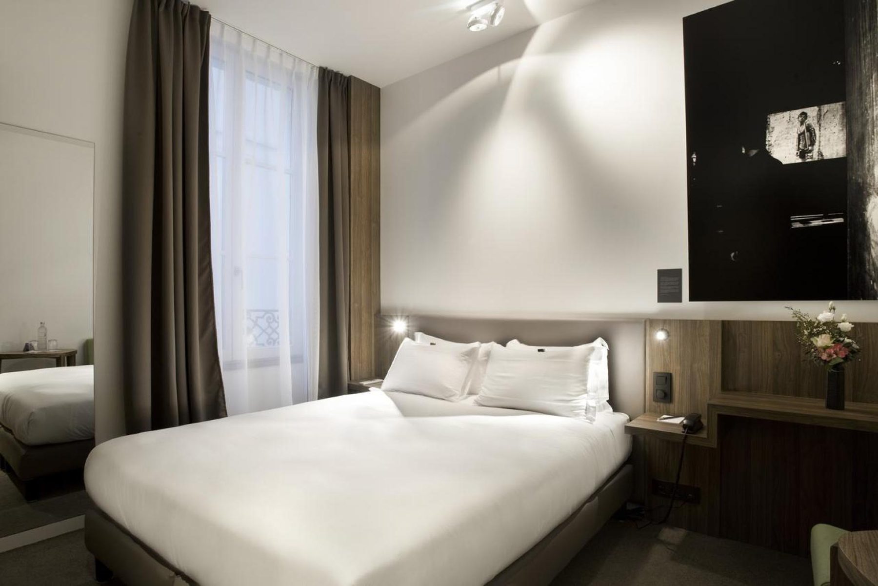 White bed, timber headboard and a black-and-white wall photograph at Hôtel Jules & Jim.