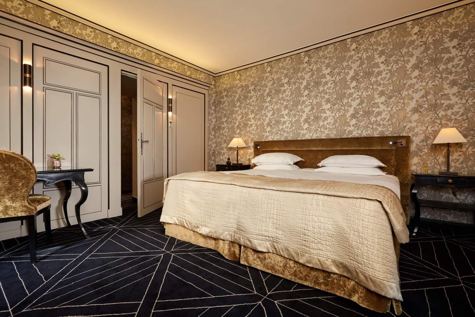 Deluxe bedroom with patterned walls and a cream bed at Le Pavillon de la Reine.