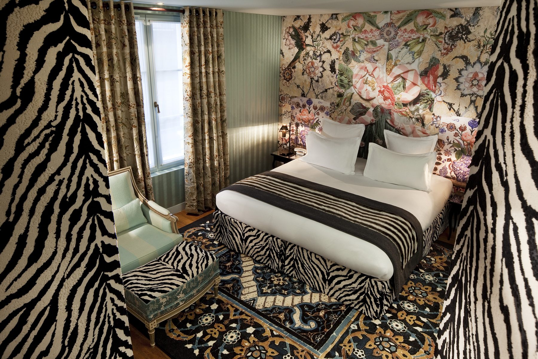 Deluxe bedroom with floral walls and zebra-patterned seating at Hôtel du Petit Moulin.