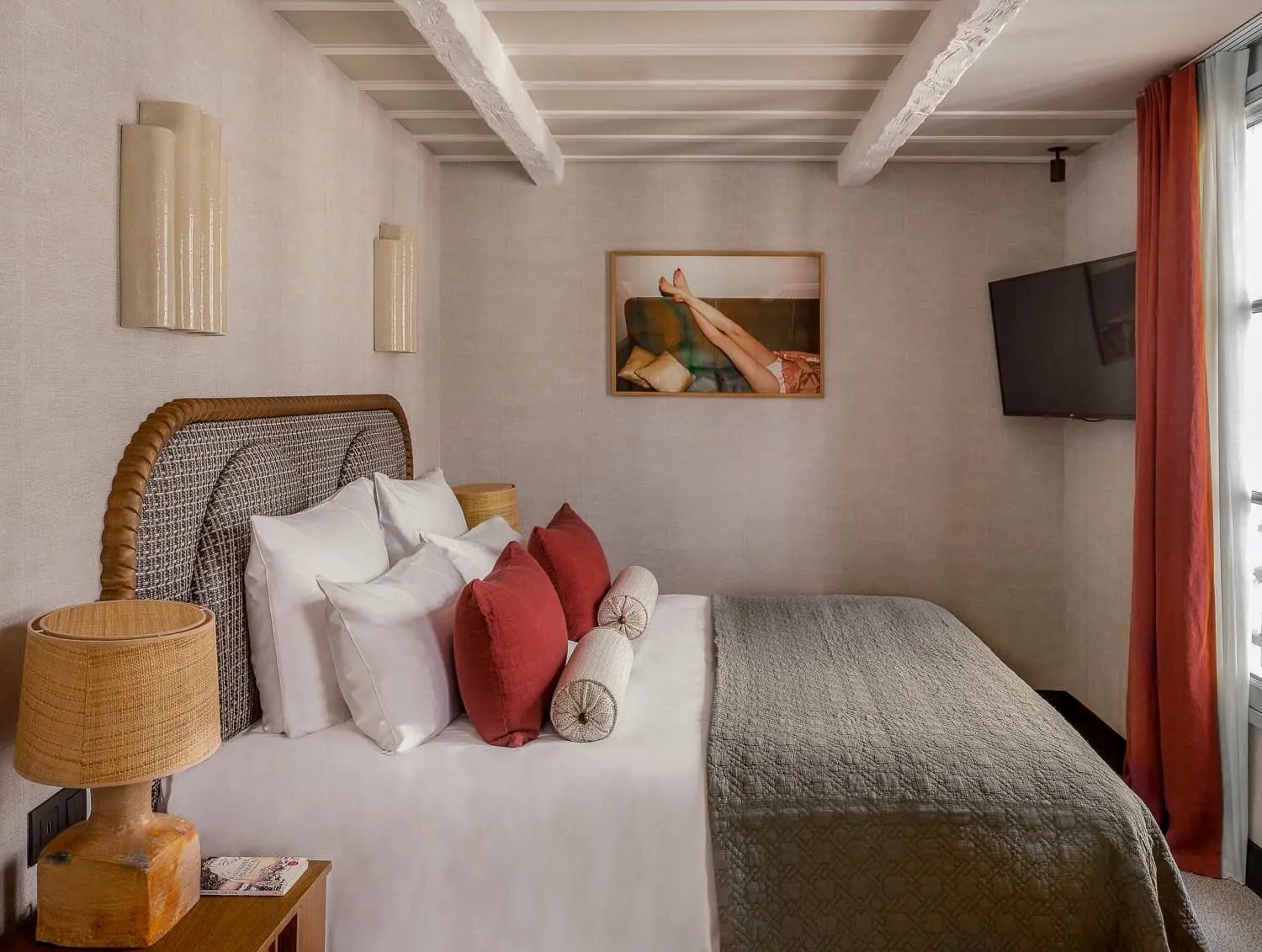 Bedroom with a woven headboard, exposed beams and red cushions at Hôtel Suzie Blue.