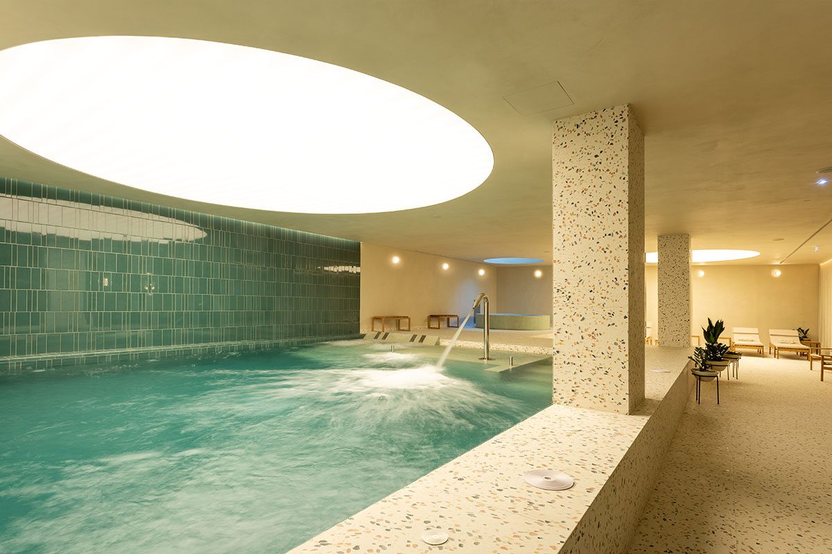Indoor pool under a large oval ceiling light with pale stone columns at Altis Porto.