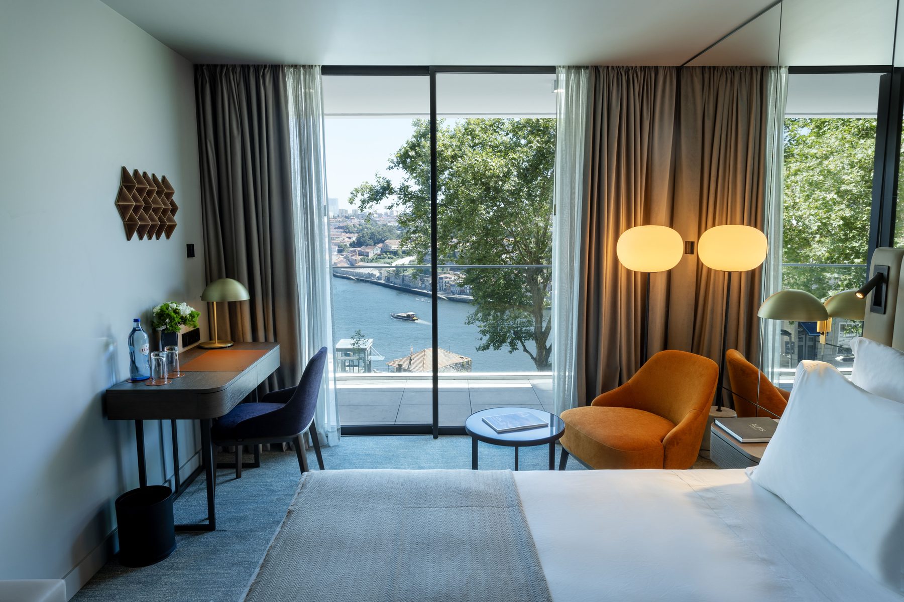 Bed, desk and orange armchair beside glazed doors facing the river at Altis Porto.