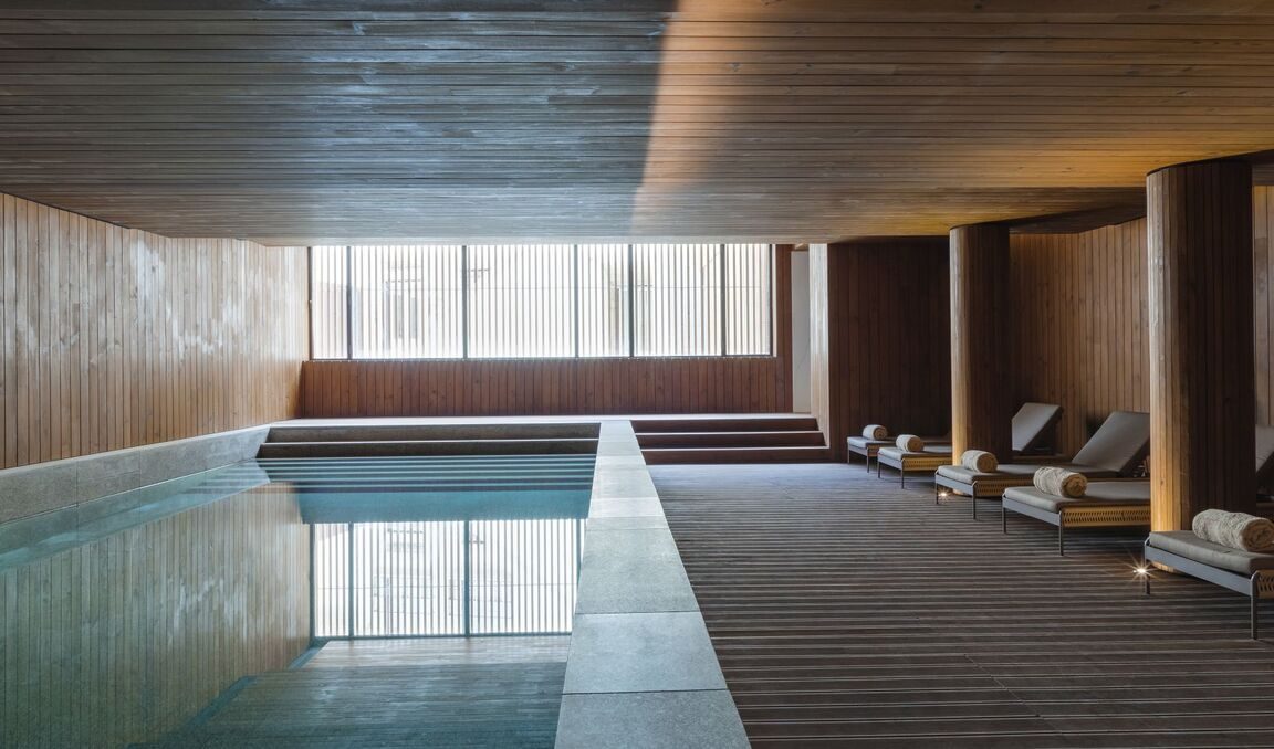 Indoor pool with timber walls, a long bench and loungers at Casa da Companhia.