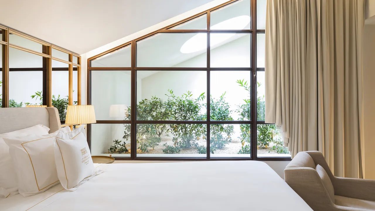 Bed beside a large black-framed glass partition and planted outdoor area at Casa da Companhia.