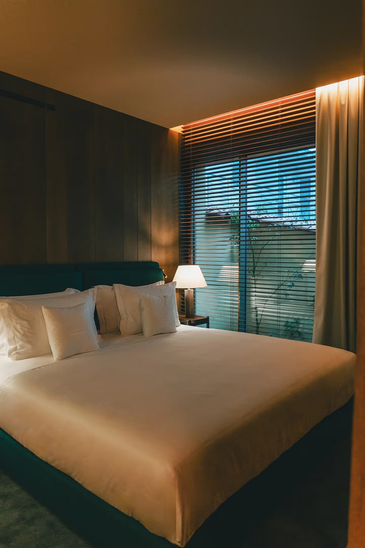 Bed and window with timber blinds in a muted green bedroom at Palacete Severo.
