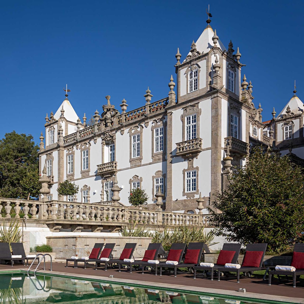 Ornate stone palace facade behind loungers and the outdoor pool at Pestana Palácio do Freixo.