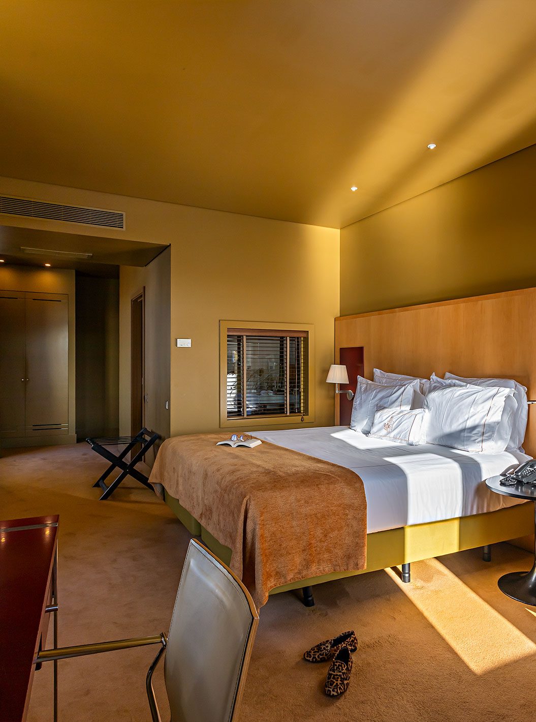 Bed with tan cover, sofa, desk and yellow walls at Pestana Palácio do Freixo.
