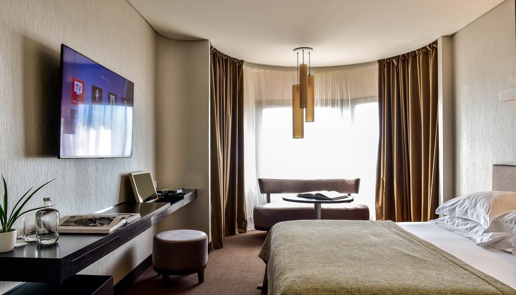 Bed, long desk, television and curved window area in a Porto Palácio Deluxe room.