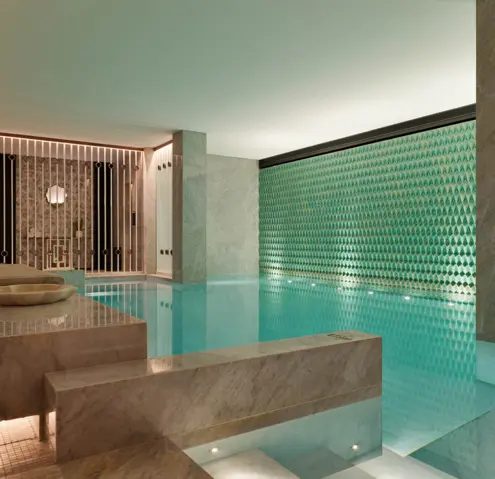 Indoor pool bordered by green mosaic walls and a timber screen at The One Monumental Palace.