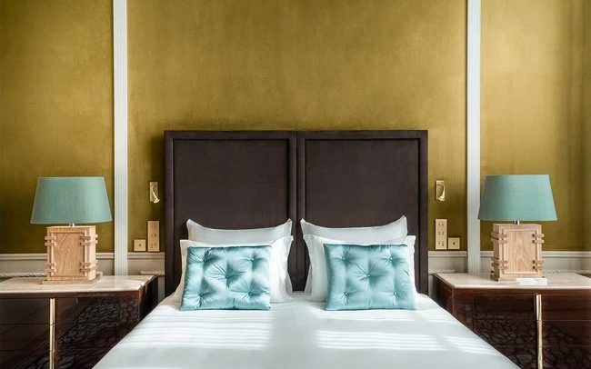 Bed with tall dark headboard, green walls and matching bedside lamps at The One Monumental Palace.