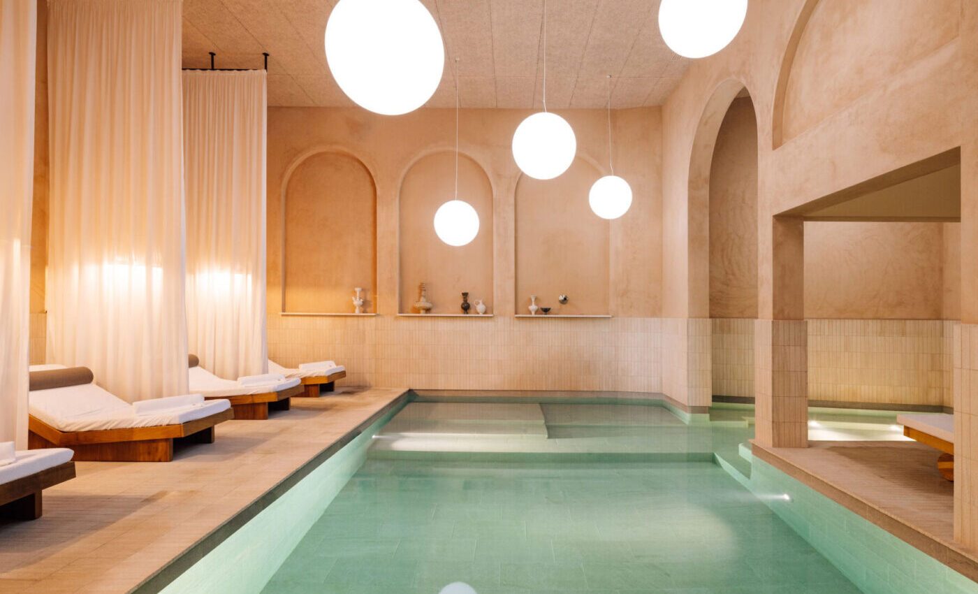 Indoor pool with warm stone walls, arches and hanging globe lights at The Rebello.