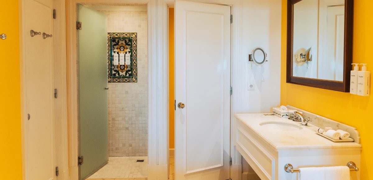 Yellow-walled bathroom with two basins and a glass shower screen at The Yeatman.