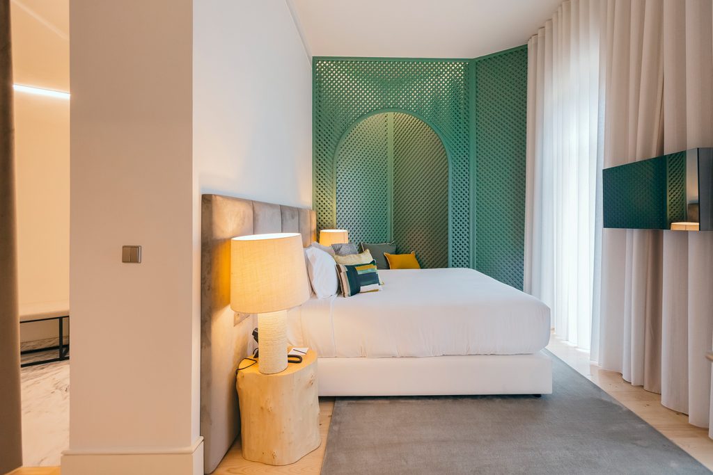 Bed, green arched headboard, pale curtains and wall-mounted television at Torel Avantgarde.