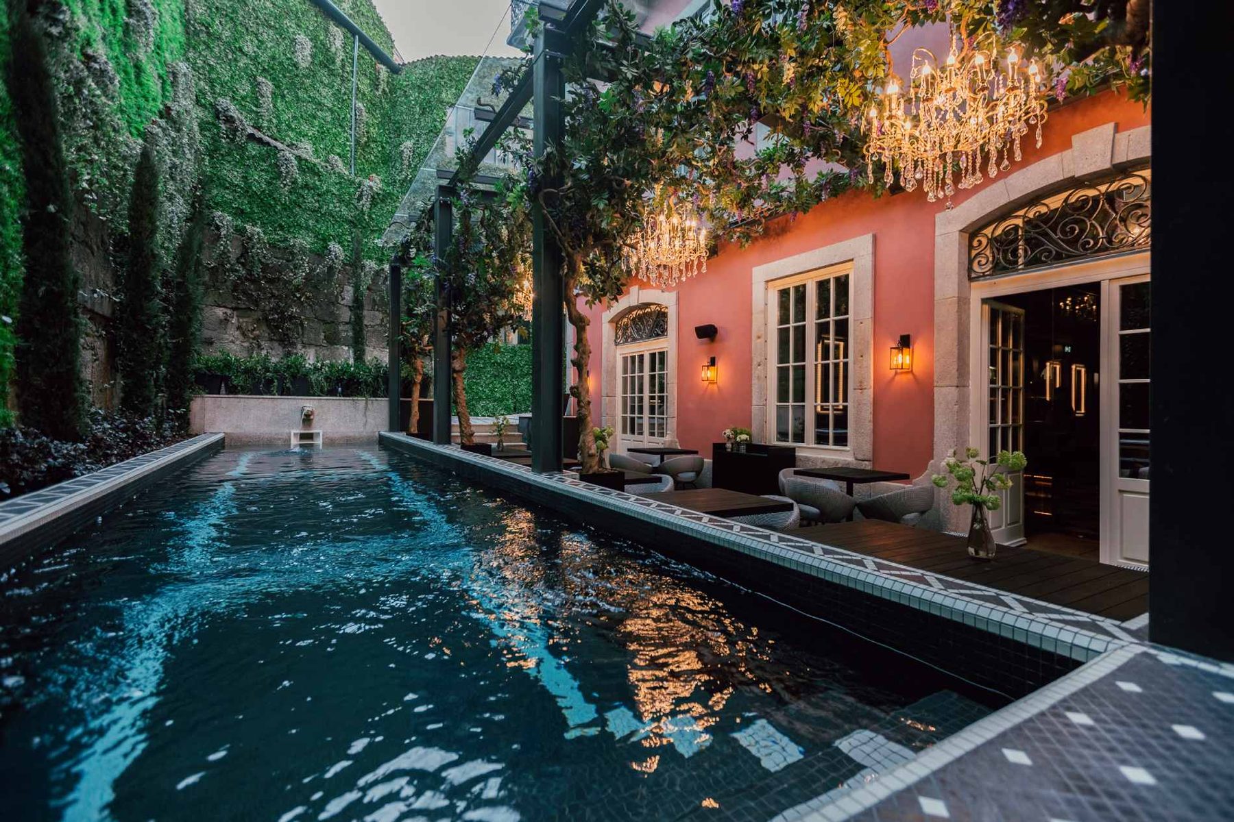 Outdoor pool beside an orange facade, foliage and hanging decorative lights at Torel Palace Porto.