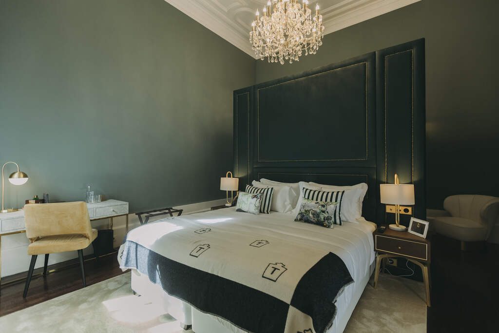 Bed against a dark green panelled wall beneath an ornate chandelier at Torel Palace Porto.