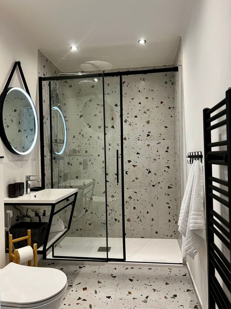 Bathroom with a glass-enclosed shower, basin and dark towel rail.