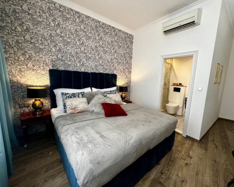 Bedroom with patterned wallpaper, a double bed and an open bathroom doorway.