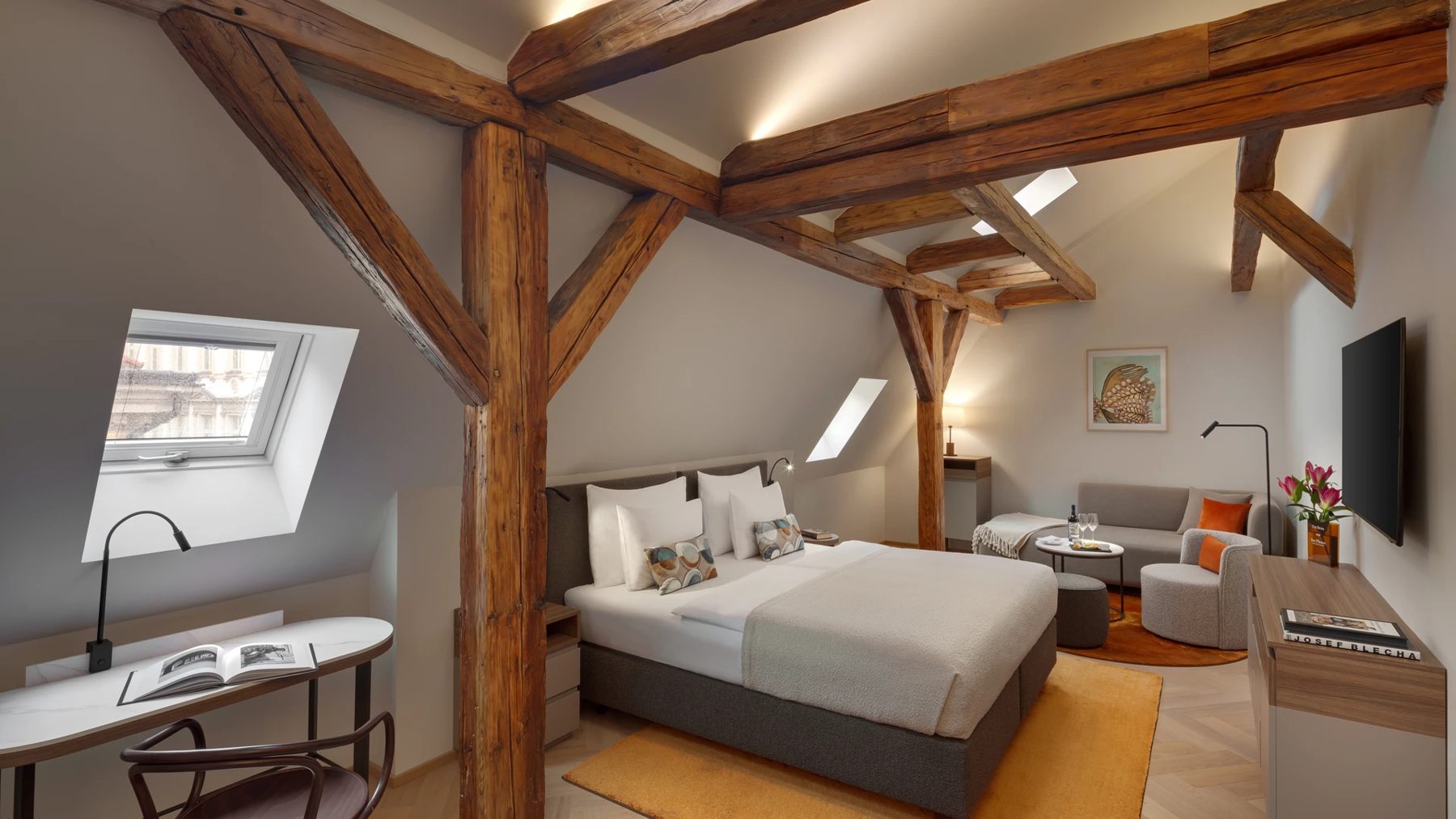Bedroom with exposed wooden beams, skylights, bed and seating.