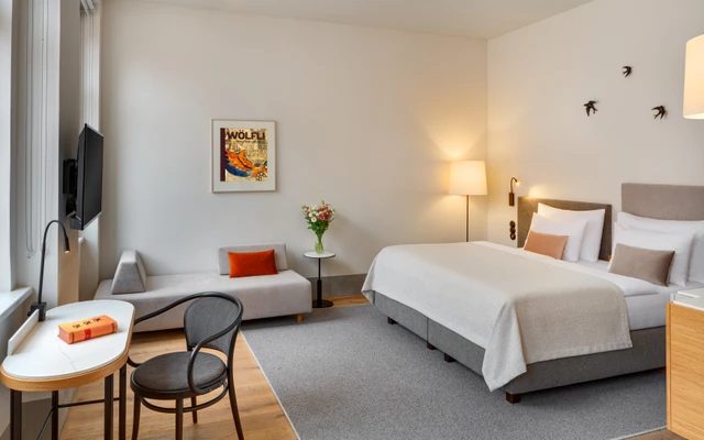 Bright bedroom with a double bed, sofa, small table and armchairs.