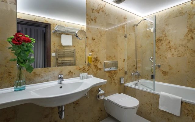 Stone-lined bathroom with a bath, glass shower screen and basin.