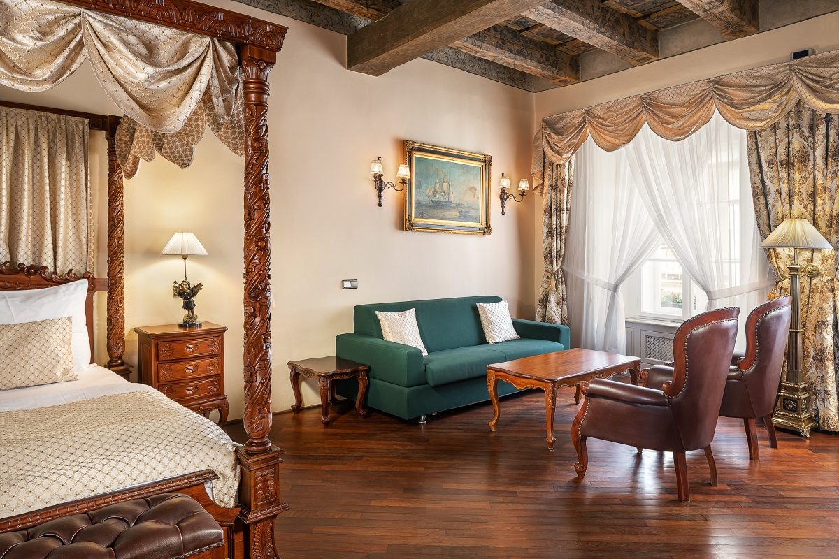 Four-poster bed beside a green sofa, armchair and exposed ceiling beams.