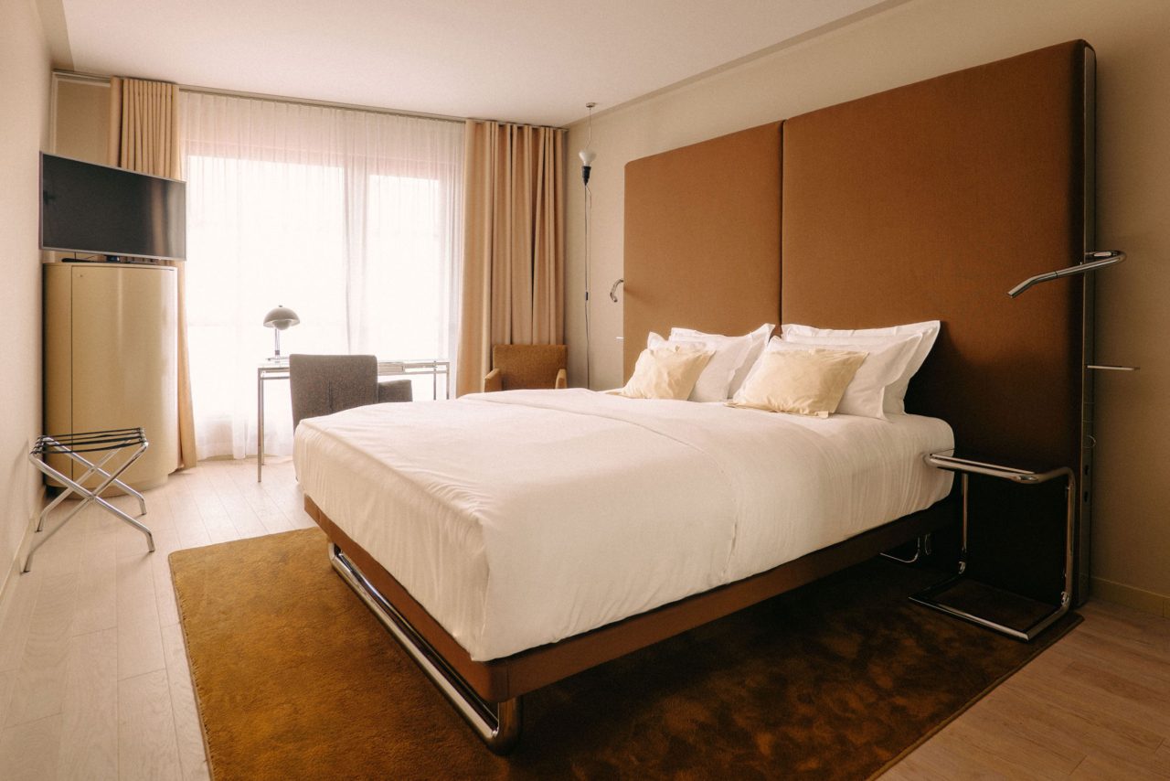 Superior bedroom with a double bed, desk and large curtained window.