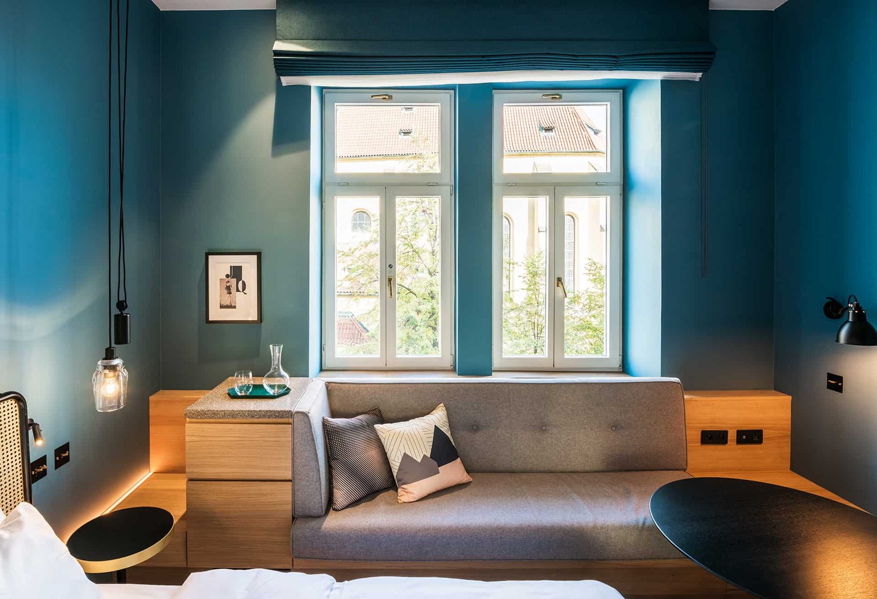 Blue-walled room with a sofa beneath a tall window and pendant lamps.