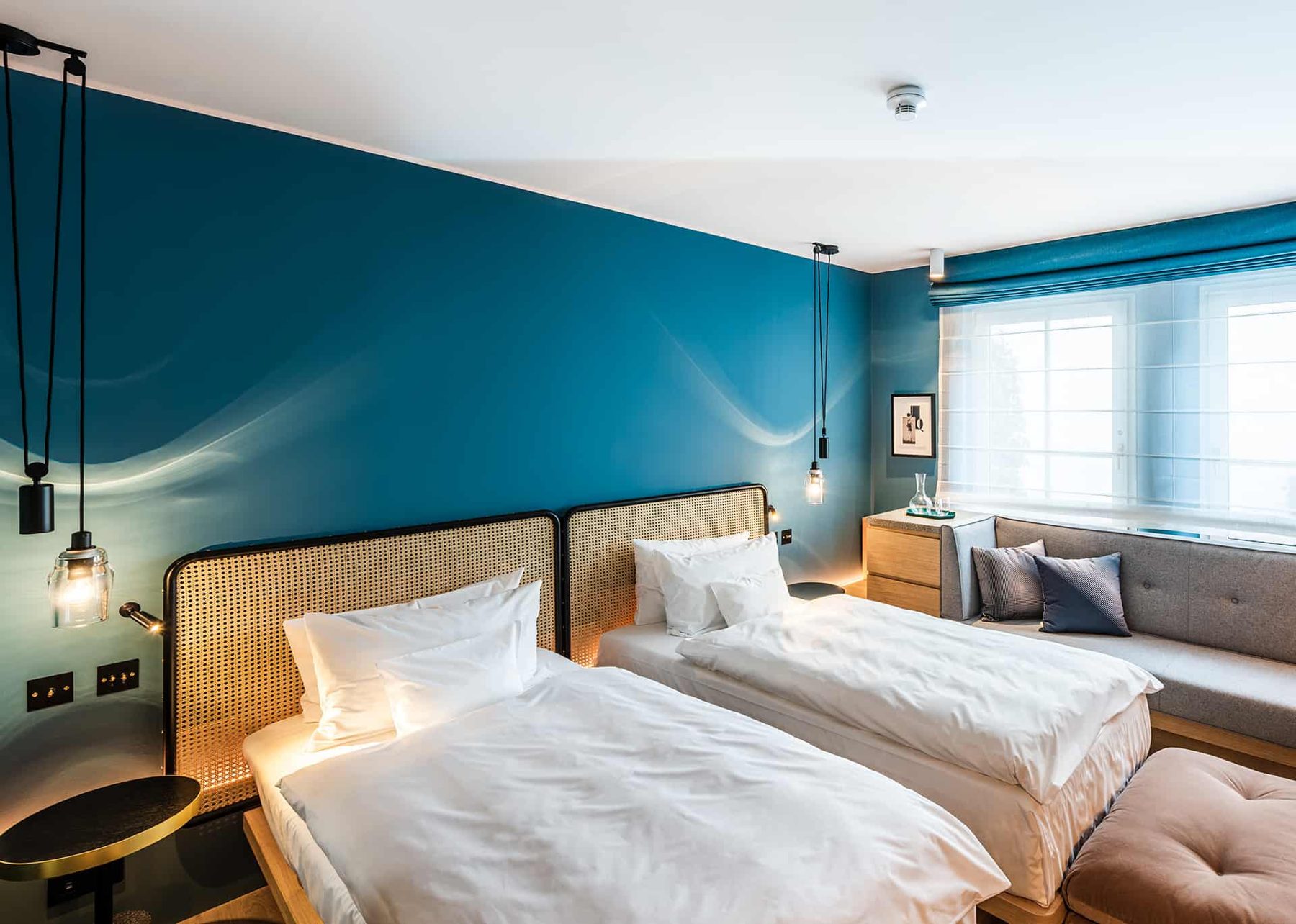 Two separate beds in a blue-walled bedroom with window-side seating.